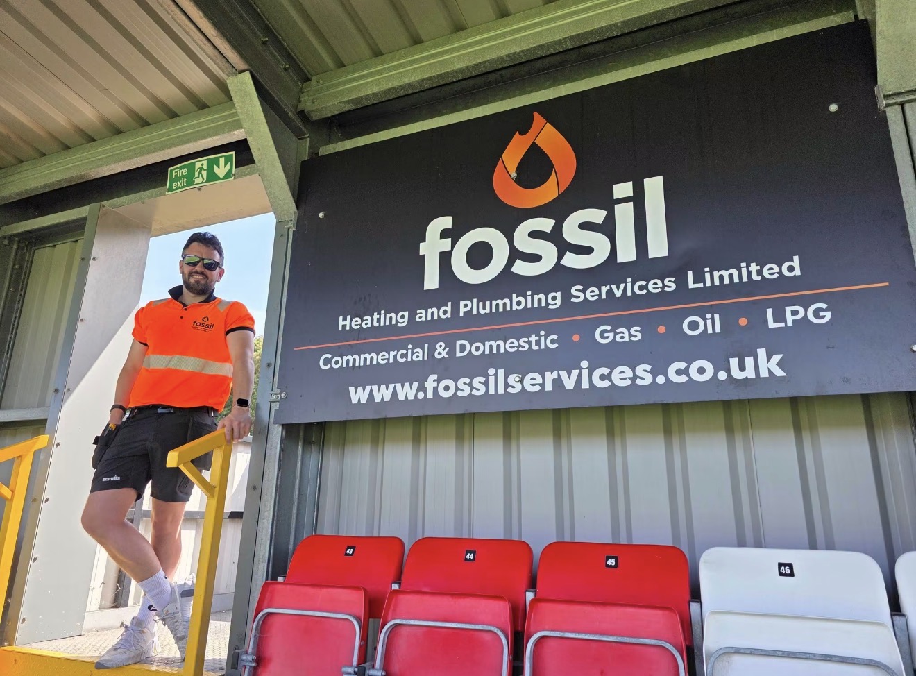 Chris Woodhouse of Fossil Heating under Fossil sponsorship signage at a stadium