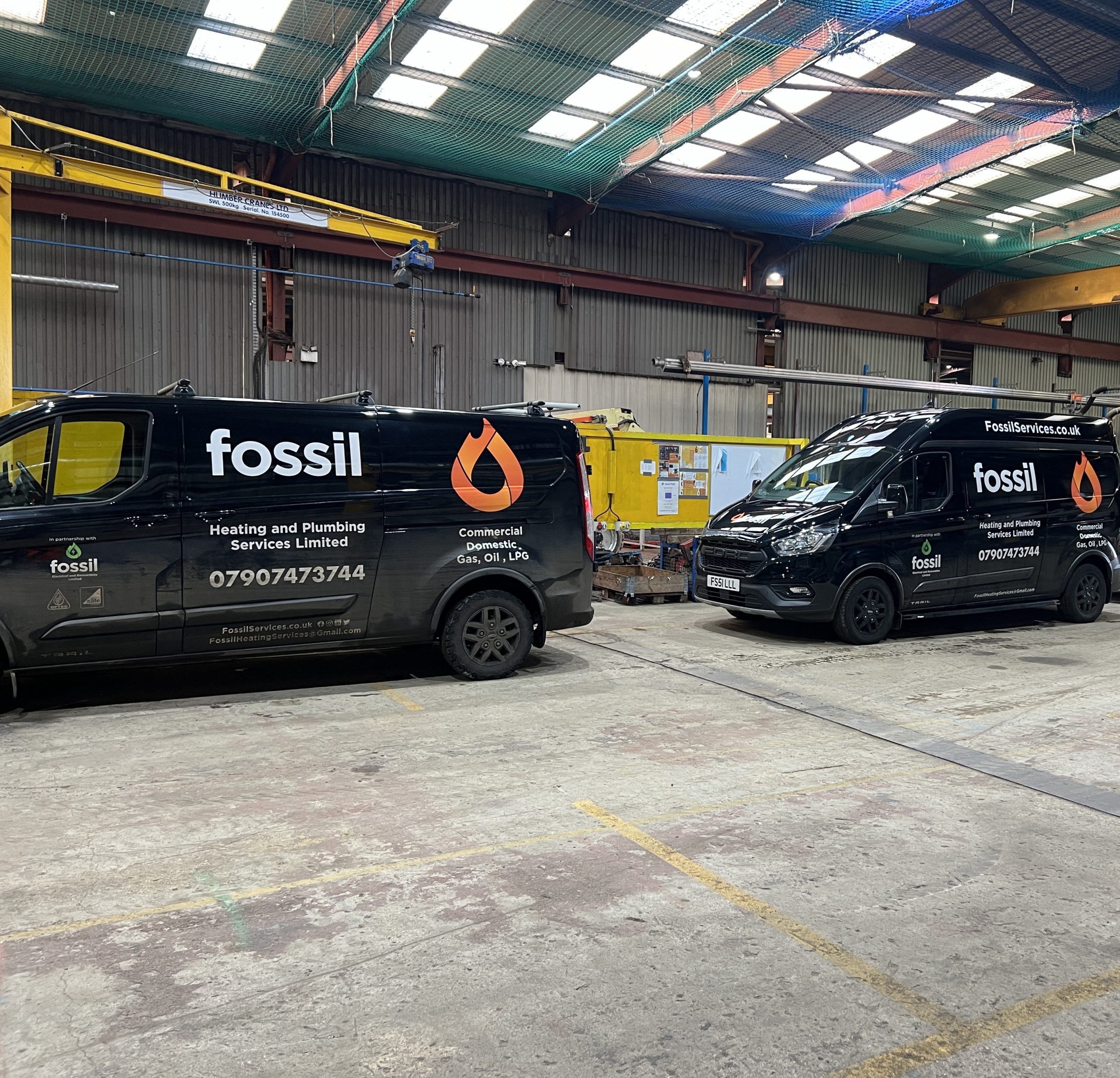Two Fossil Heating branded vans parked in the company warehouse